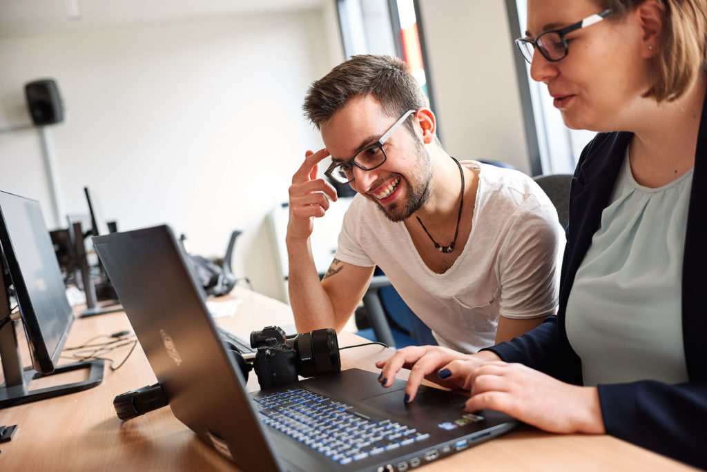 Eine Frau erklärt einem jungen Mann etwas an einem Laptop